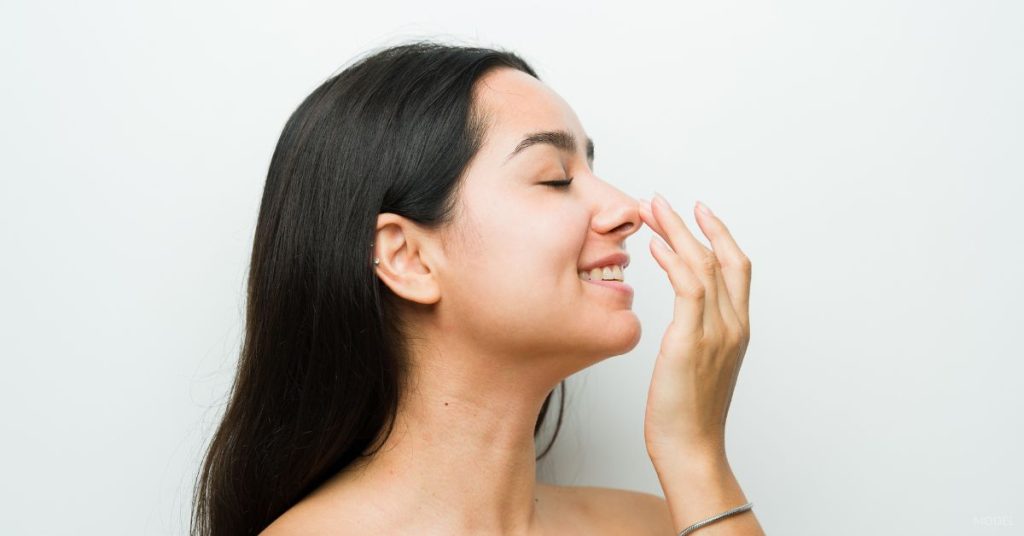 woman touching her nose admiring her rhinoplasty procedure (MODEL)